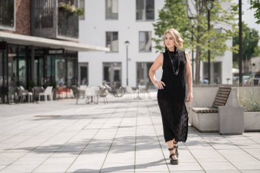 Litvanya 'daki Vilnius Old Town Caddesi. Beyaz, beyaz, yetişkin bir kadın siyah elbise ve boynuna bijouterie giyiyor. Dışarıdaki Sandalyelerle Arka planda Dükkan ve Restoran
