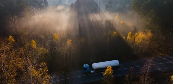 Foggy autumn morning on the road among the woods with a fuel truck passing along the road — Stock Photo, Image