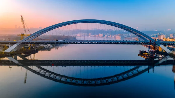 Повітряний вид на новий залізничний міст, який відбивається над спокійною річкою Дніпро до світанку в центрі міста. Схід сонця над Києвом, Україна. — стокове фото