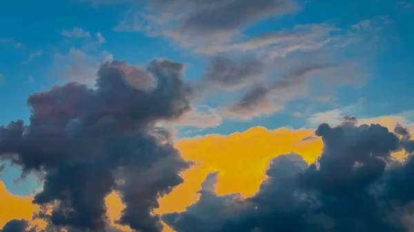 Akşamları koyu gri ve sarı bulutlar batan güneşin ışınlarında mavi gökyüzü