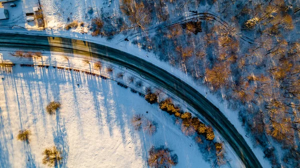 İlk karla kaplı soğuk kış ormanları ve koruluklardan geçen yolun virajının drone fotoğrafı.. — Stok fotoğraf