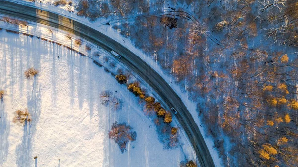 İlk karla kaplı soğuk kış ormanları ve koruluklardan geçen yolun virajının drone fotoğrafı..