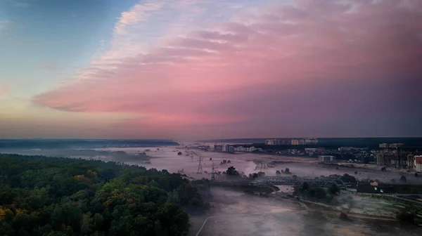 Şafaktan önce kuş bakışı görülebilen sisli bir tarla. Açık ve kasvetli pembe-mor gökyüzü.