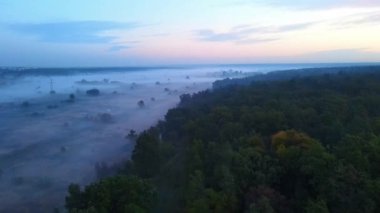 Şafaktan önce kuş bakışı görülebilen sisli bir tarla. Açık ve kasvetli pembe-mor gökyüzü.