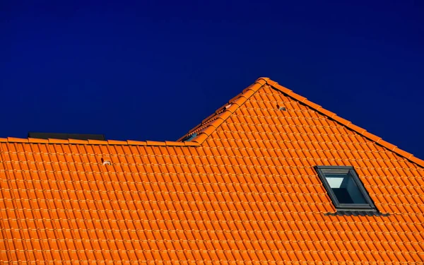 หน้าต่างบนหลังคาของบ้านที่มีกระเบื้องหลังคาสีส้มบนพื้นหลังของท้องฟ้าสีฟ้า — ภาพถ่ายสต็อก