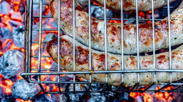 Sausage. Fried meat sausages on a grill grate on the background of hot coals. Juicy sausages on coals. View from above. High quality photo.