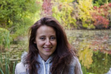 Genç neşeli kız portresi gölde ya da nehirde mevsimlik tabiatı ve ağaçlardaki renkli yapraklarla parkta ya da ormanda.