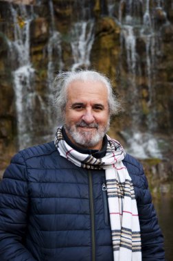 Sonbahar ceketi ve şelalenin arka planında atkısı olan mutlu kır saçlı adam..