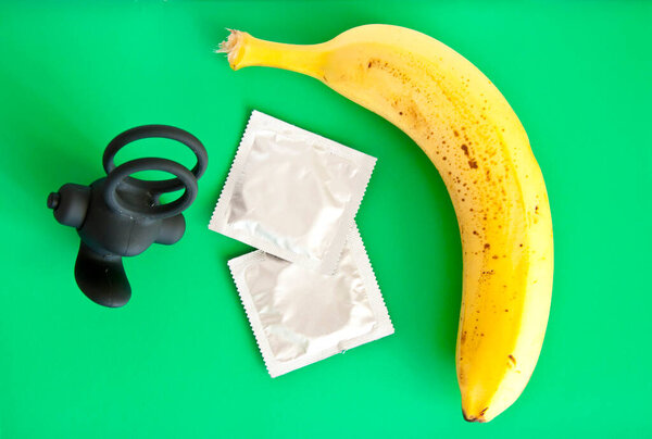condom with banana and penis ring on green background.
