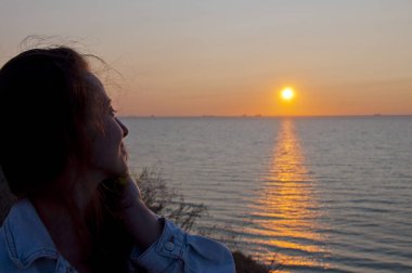 Kızın silueti yaz güneşine ve deniz manzaralı gökyüzüne bakıyor. Boşluğu kopyala.