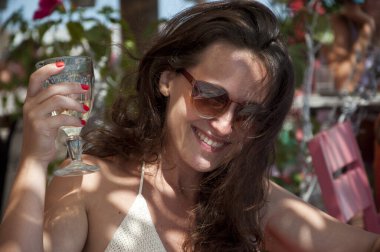 Neşeli genç kadın güneş gözlüğü takıyor. Yaz restoranında tatil köyünde şarap içiyor..