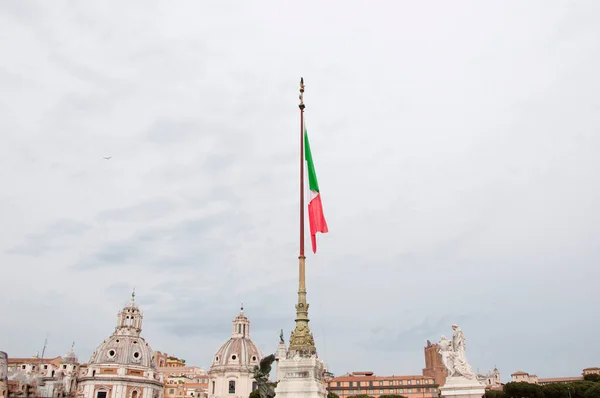 National flag of Italian republic il Tricolore waving on flagpole over ancient Rome cityscape sky background.