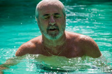 senior man swimming in summer pool on summertime vacation.
