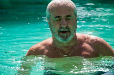 old man swimming in summer pool on summertime vacation.