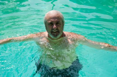 retired man swimming in summer pool on summertime vacation.