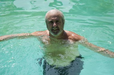 cheerful senior man swimming in summer pool on summertime vacation.