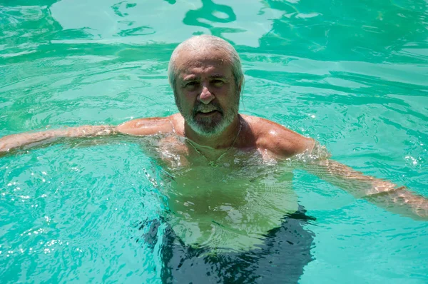 cheerful senior man swimming in summer pool on summertime vacation.