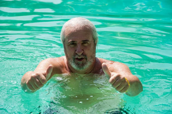 aged man swimming in summer pool on summertime vacation. thumb up.