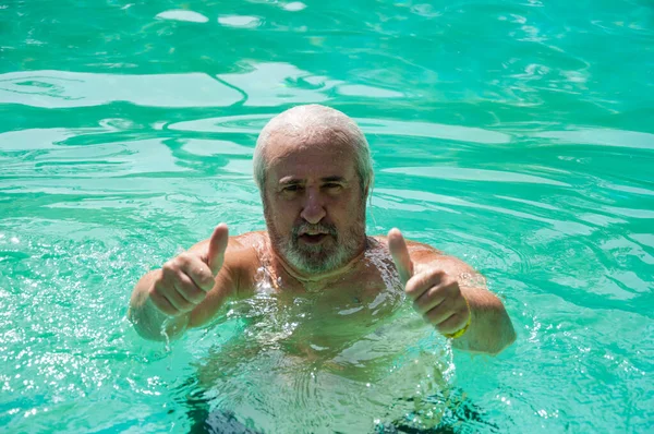 senior man swimming in summer pool on summertime vacation. thumb up.