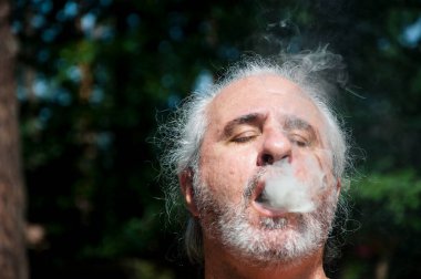 senior man enjoying smoking at summer vacation and suntan. smoke and copy space.