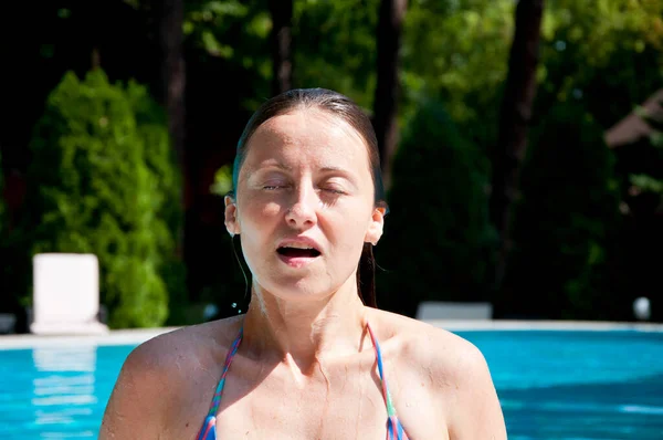 woman with wet face in summer pool water on vacation.