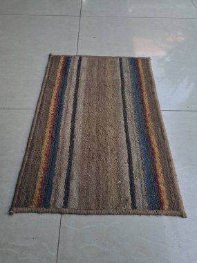 Kahverengi, kırmızı, mavi çizgili paspas beyaz, porselen bir zeminde.