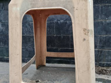 Açık kahverengi plastik sandalye bacakları bina duvarının önünde.