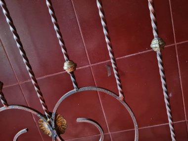 Altın kahverengi demir çitin arka planı kırmızı porselen duvarın ve beyaz duvar boyasının önünde desenlenmiştir.