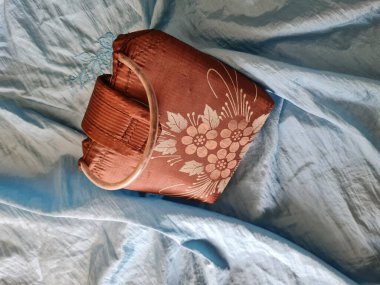 Açık mavi kumaş arka planda plastik saplı güzel kahverengi bir çiçek çantası.