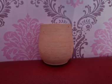 Duvarında pembe bir süs olan kahverengi topraktan yapılmış bir sürahi.