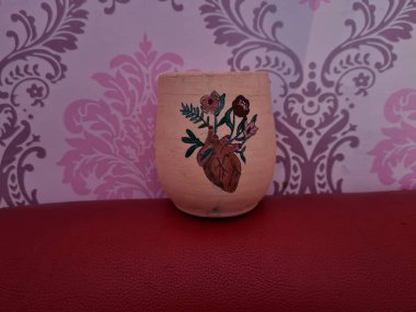 Duvarında pembe bir süs olan kahverengi topraktan yapılmış bir sürahi.