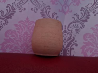 Duvarında pembe bir süs olan kahverengi topraktan yapılmış bir sürahi.