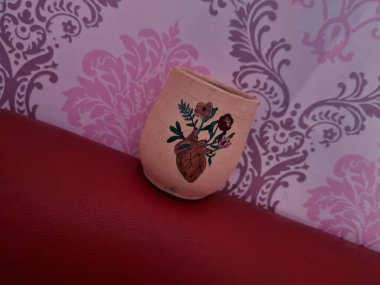 Duvarında pembe bir süs olan kahverengi topraktan yapılmış bir sürahi.