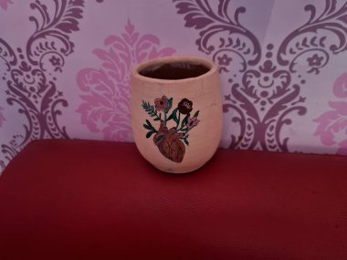 Duvarında pembe bir süs olan kahverengi topraktan yapılmış bir sürahi.