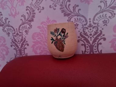 Duvarında pembe bir süs olan kahverengi topraktan yapılmış bir sürahi.