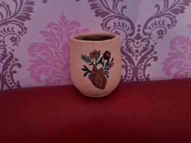 Duvarında pembe bir süs olan kahverengi topraktan yapılmış bir sürahi.