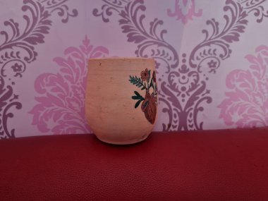 Duvarında pembe bir süs olan kahverengi topraktan yapılmış bir sürahi.