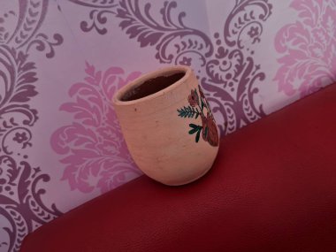 Duvarında pembe bir süs olan kahverengi topraktan yapılmış bir sürahi.