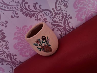 Duvarında pembe bir süs olan kahverengi topraktan yapılmış bir sürahi.