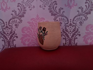 Duvarında pembe bir süs olan kahverengi topraktan yapılmış bir sürahi.
