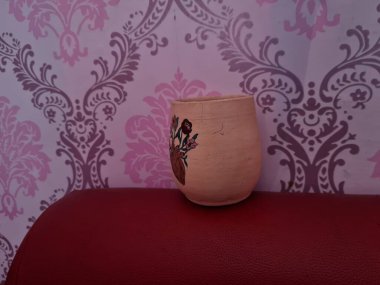 Duvarında pembe bir süs olan kahverengi topraktan yapılmış bir sürahi.