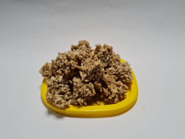 Rengginang denilen hafif bir atıştırmalık un ve sarı bir kabın içindeki diğer koyu kahverengi malzemelerden yapılır.