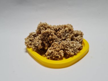 Rengginang denilen hafif bir atıştırmalık un ve sarı bir kabın içindeki diğer koyu kahverengi malzemelerden yapılır.