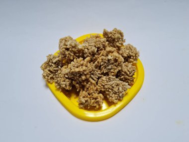 Rengginang denilen hafif bir atıştırmalık un ve sarı bir kabın içindeki diğer koyu kahverengi malzemelerden yapılır.