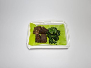 Beyaz kabın içinde yeşil sebzeli kızarmış et dilimleri.