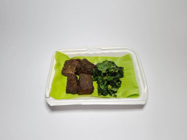 Beyaz kabın içinde yeşil sebzeli kızarmış et dilimleri.