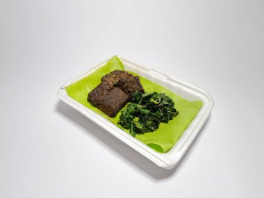 Beyaz kabın içinde yeşil sebzeli kızarmış et dilimleri.