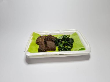 Beyaz kabın içinde yeşil sebzeli kızarmış et dilimleri.