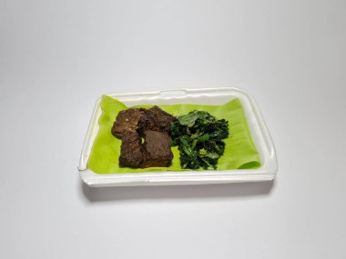 Beyaz kabın içinde yeşil sebzeli kızarmış et dilimleri.