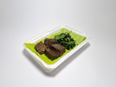 Beyaz kabın içinde yeşil sebzeli kızarmış et dilimleri.